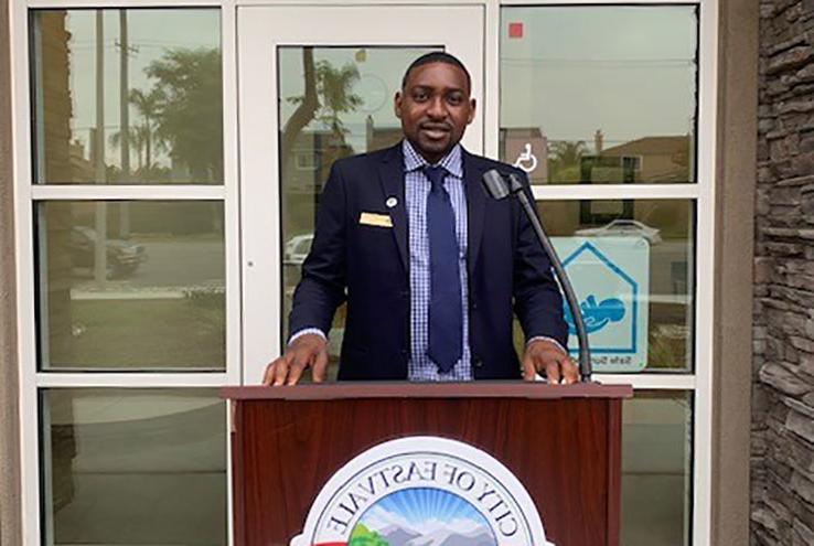 Ibraheem Lawal at the podium in front of the City of Eastvale City Hall building.